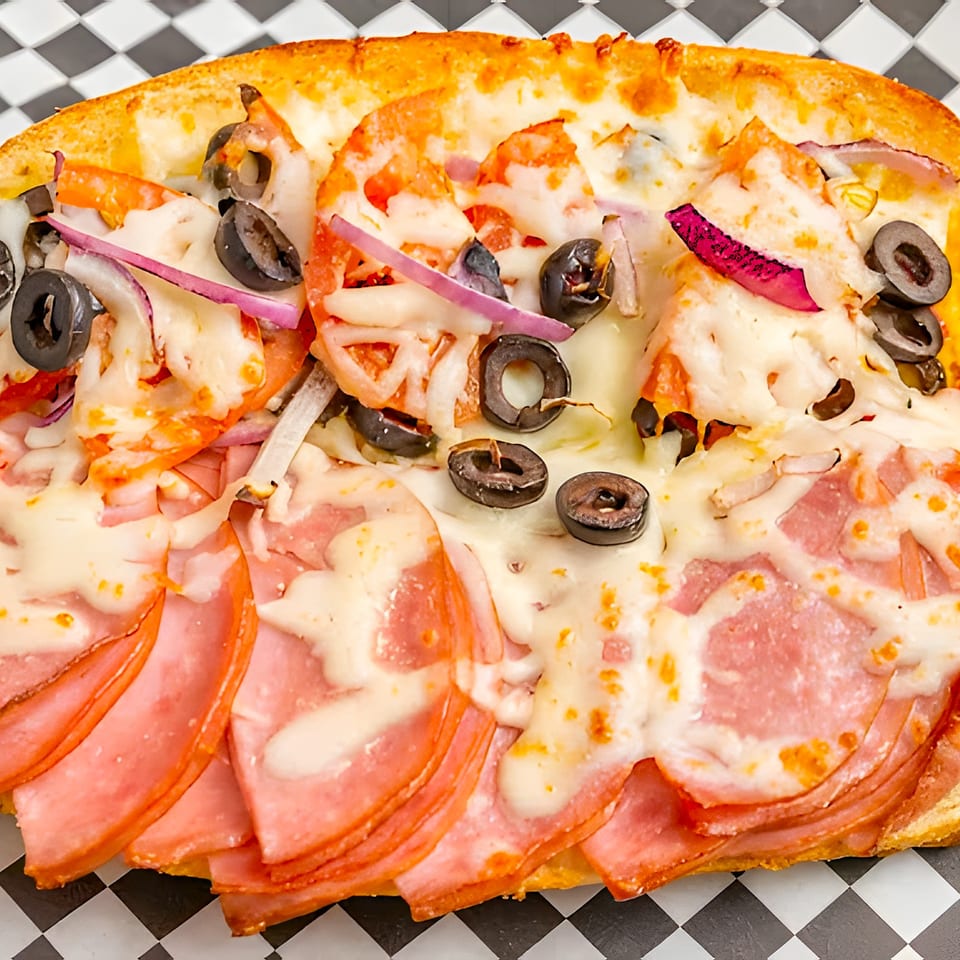 A close-up of a Pizza Pizazz pizza with ham, olives, red onions, and tomatoes.