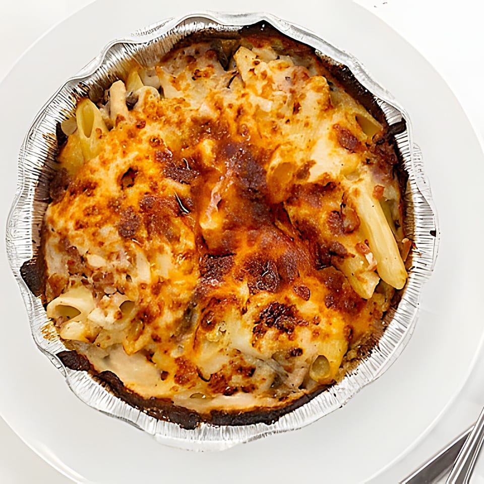 Baked penne pasta with melted cheese in a foil container on a white plate.