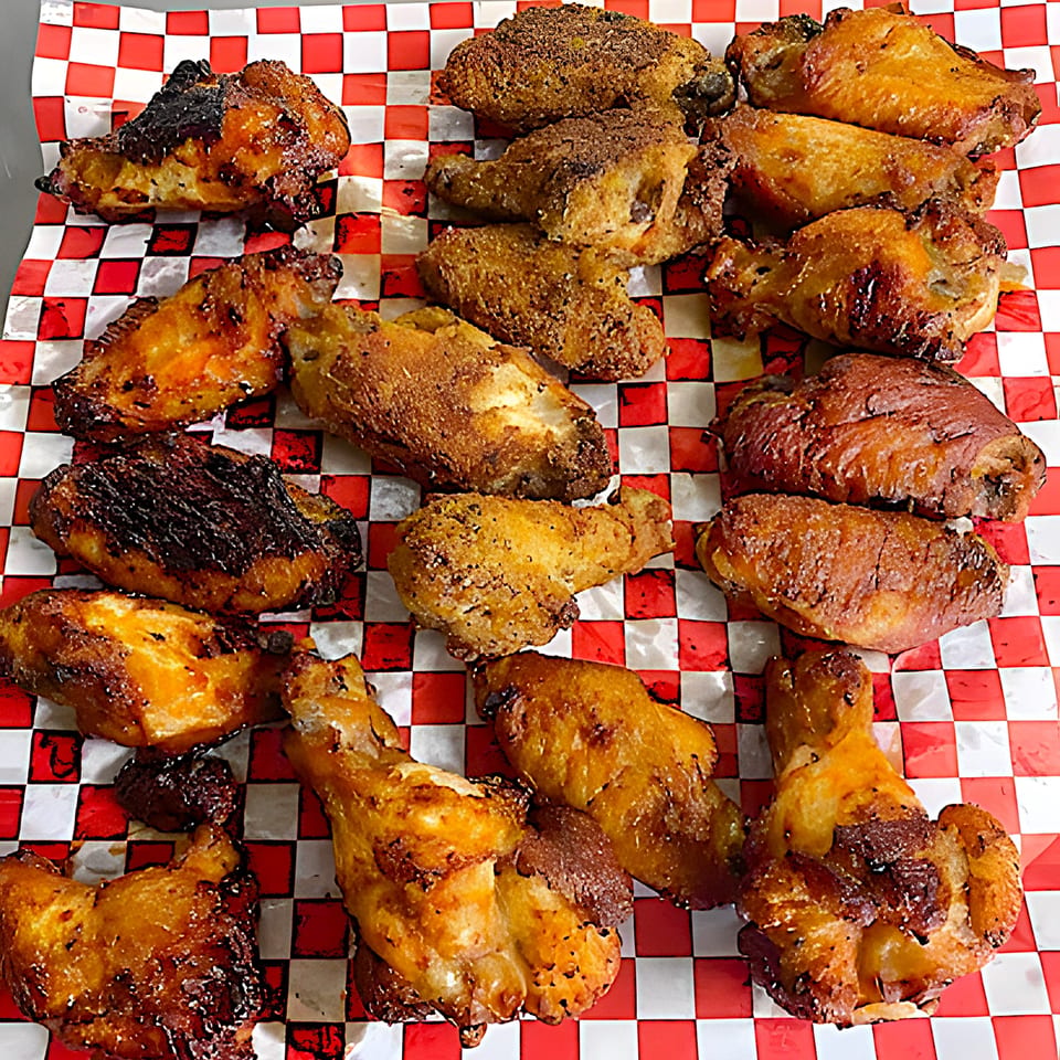A variety of golden-brown chicken wings, some crispy and some saucy, on red and white checkered paper.