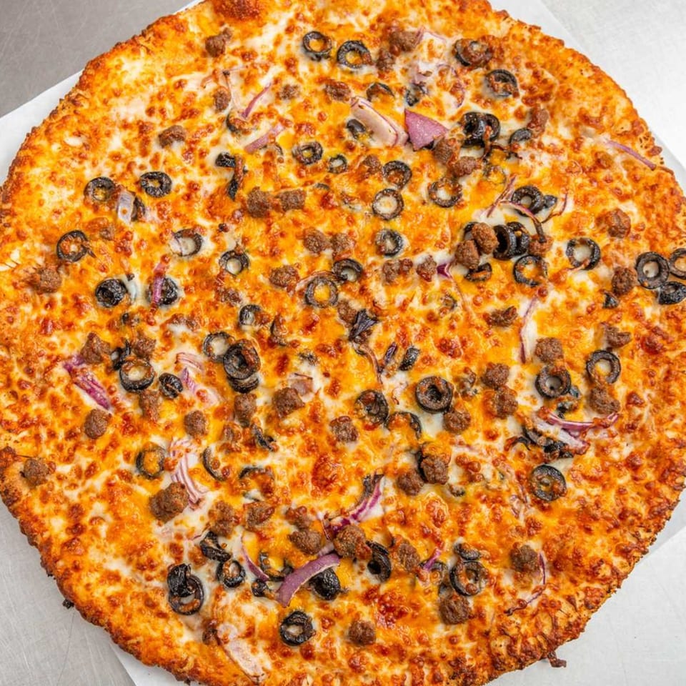 A whole Pizza Pizazz pizza, topped with melted cheese, sausage, black olives, and red onions.
