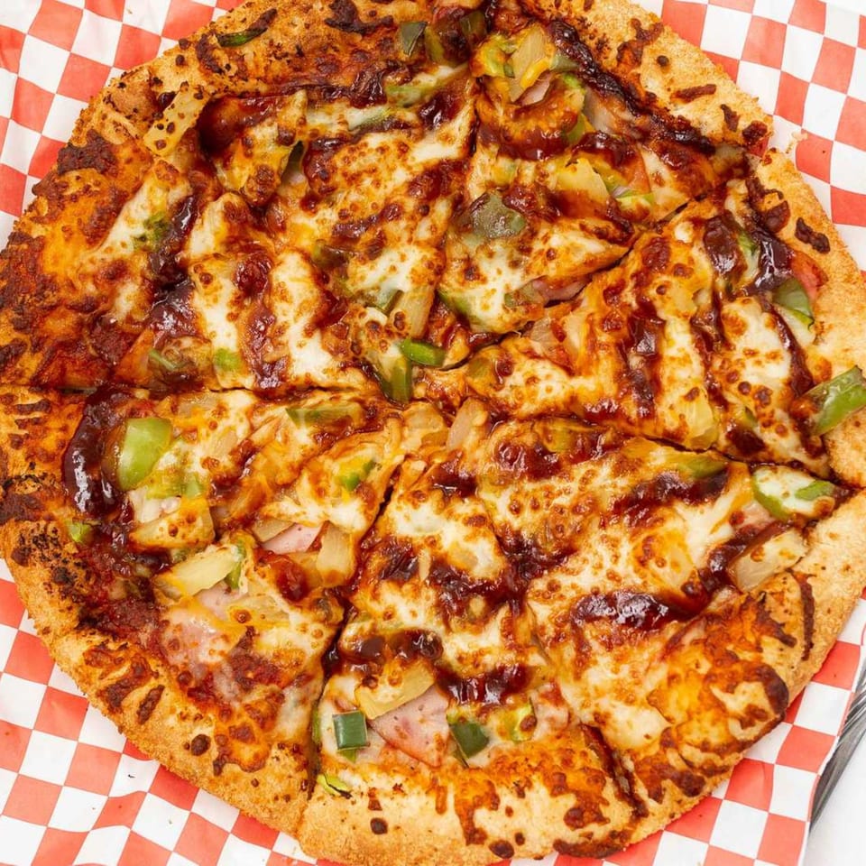A whole Pizza Pizazz pizza with BBQ sauce, cheese, green peppers, pineapple, and ham.